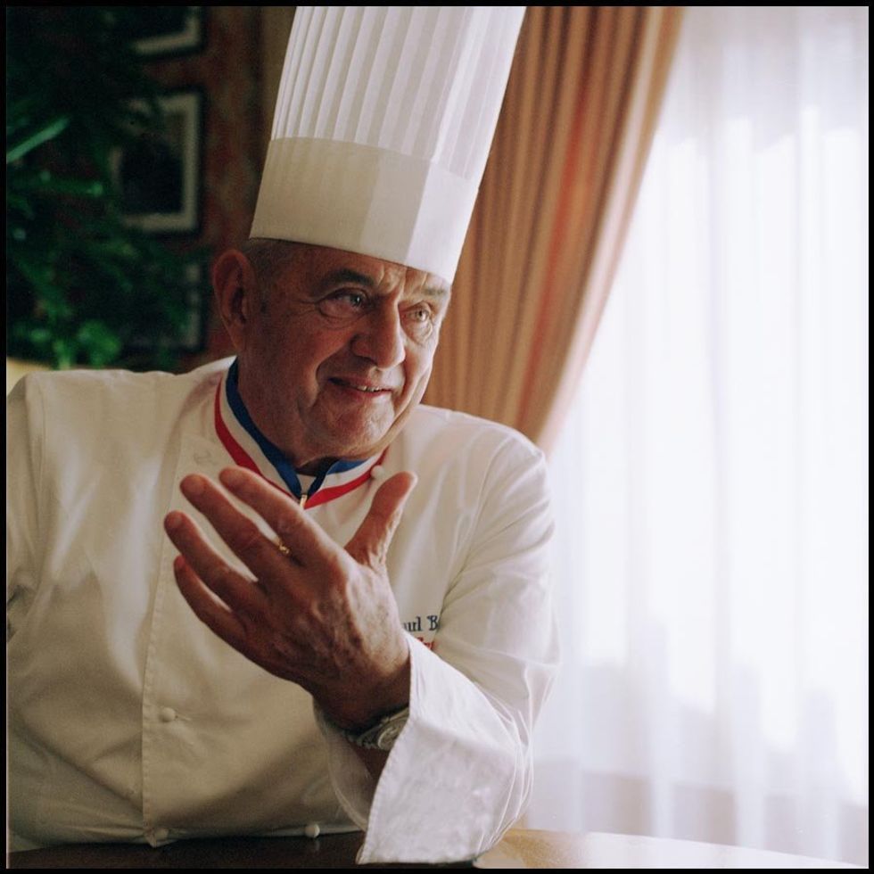 Paul Bocuse leans on a table, dressed in chef's whites