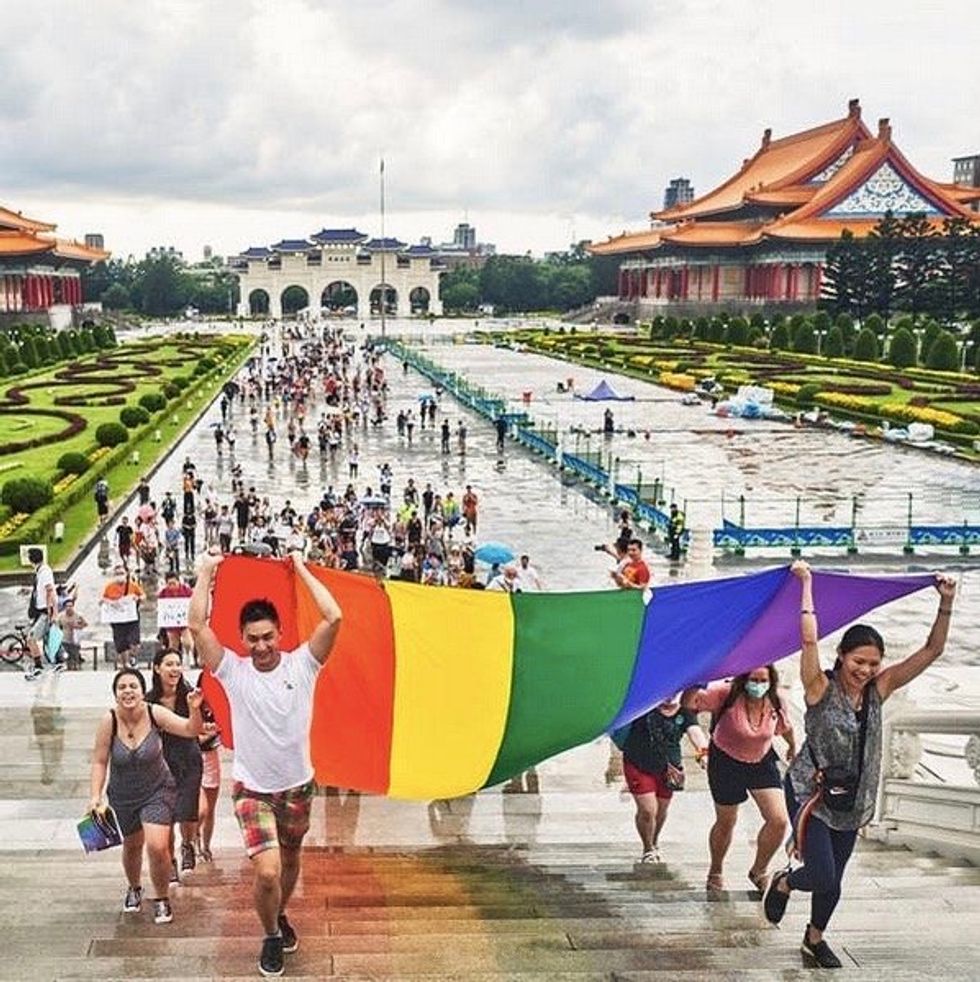 People attending Taipei Pride walk a giant rainbow flag up the stairs
