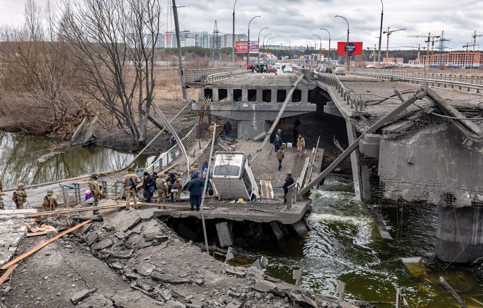 People cross a destroyed bridge as they evacuate the city of Irpin