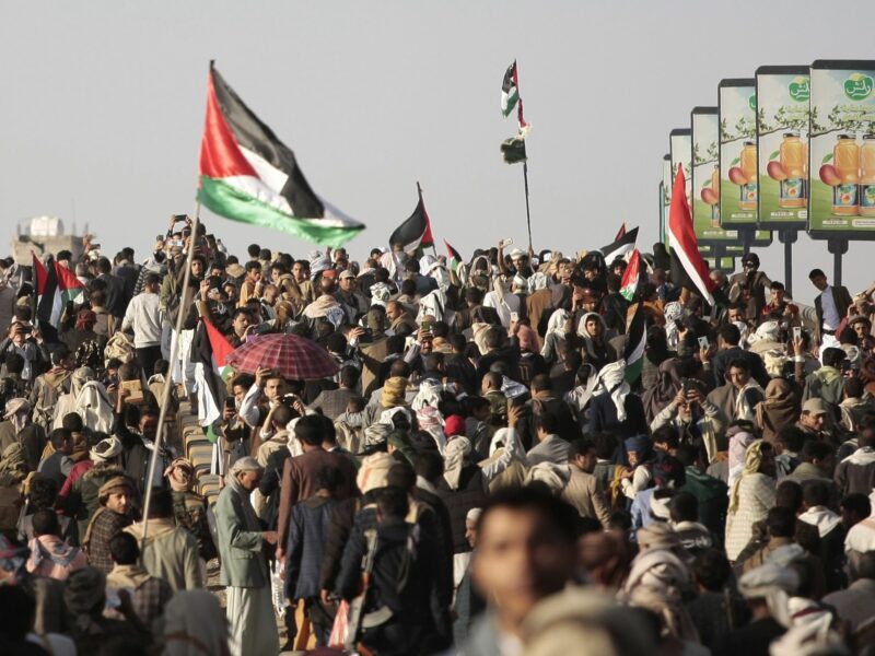 people hold up guns, wave a Palestinian flag and chant slogans during demonstrate against multinational operation to safeguard Red Sea shipping , following US and UK airstrikes on Houthis military sites, in Sana'a, Yemen.