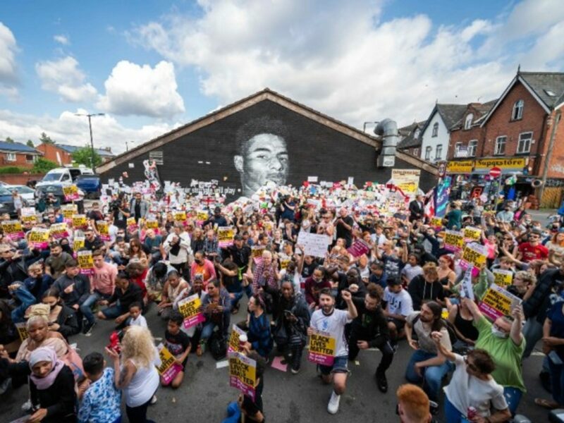 People kneel in front of a mural of Manchester United striker Marcus Rashford