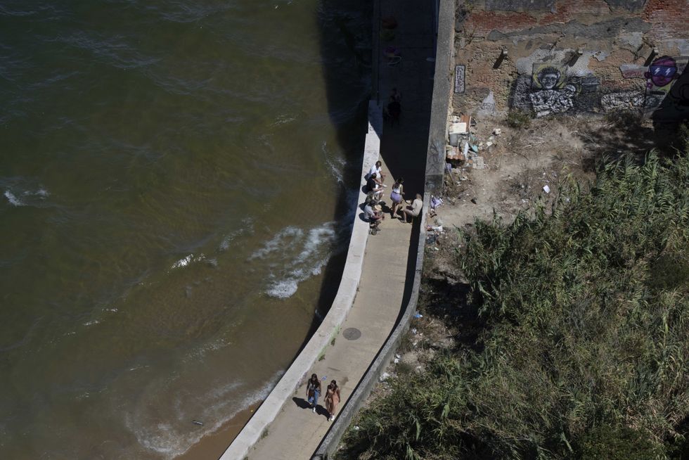 People seen walking along a promenade near the Tejo river in the town of Alamada.