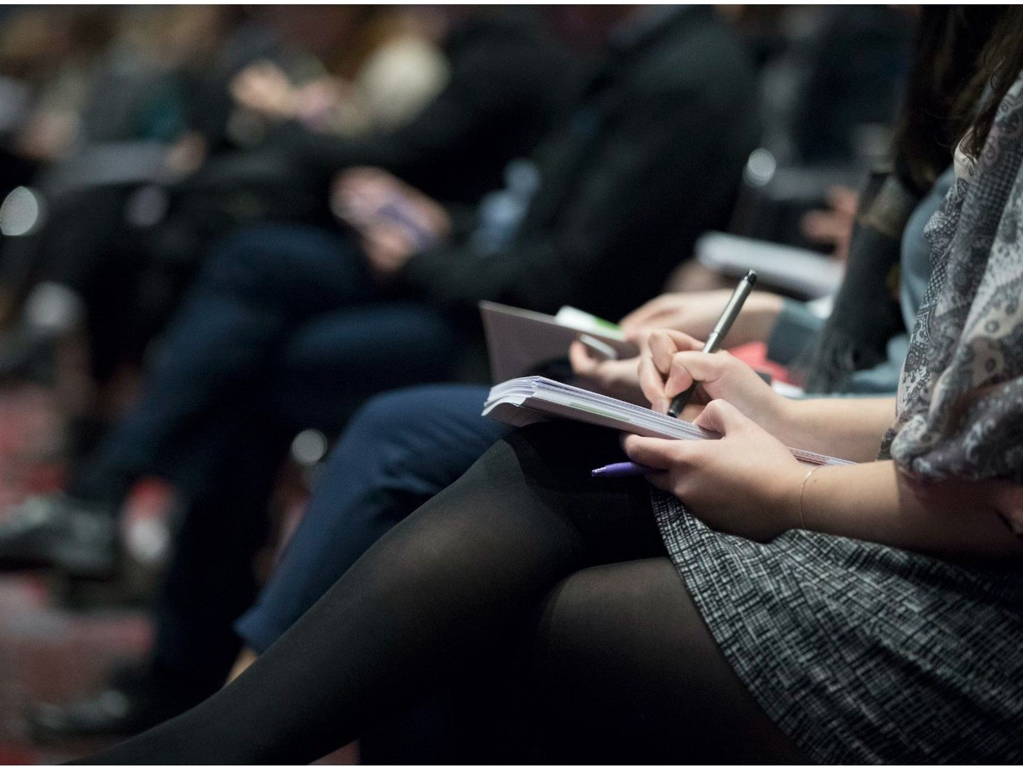 People sitting on chairs while writing on notebooks