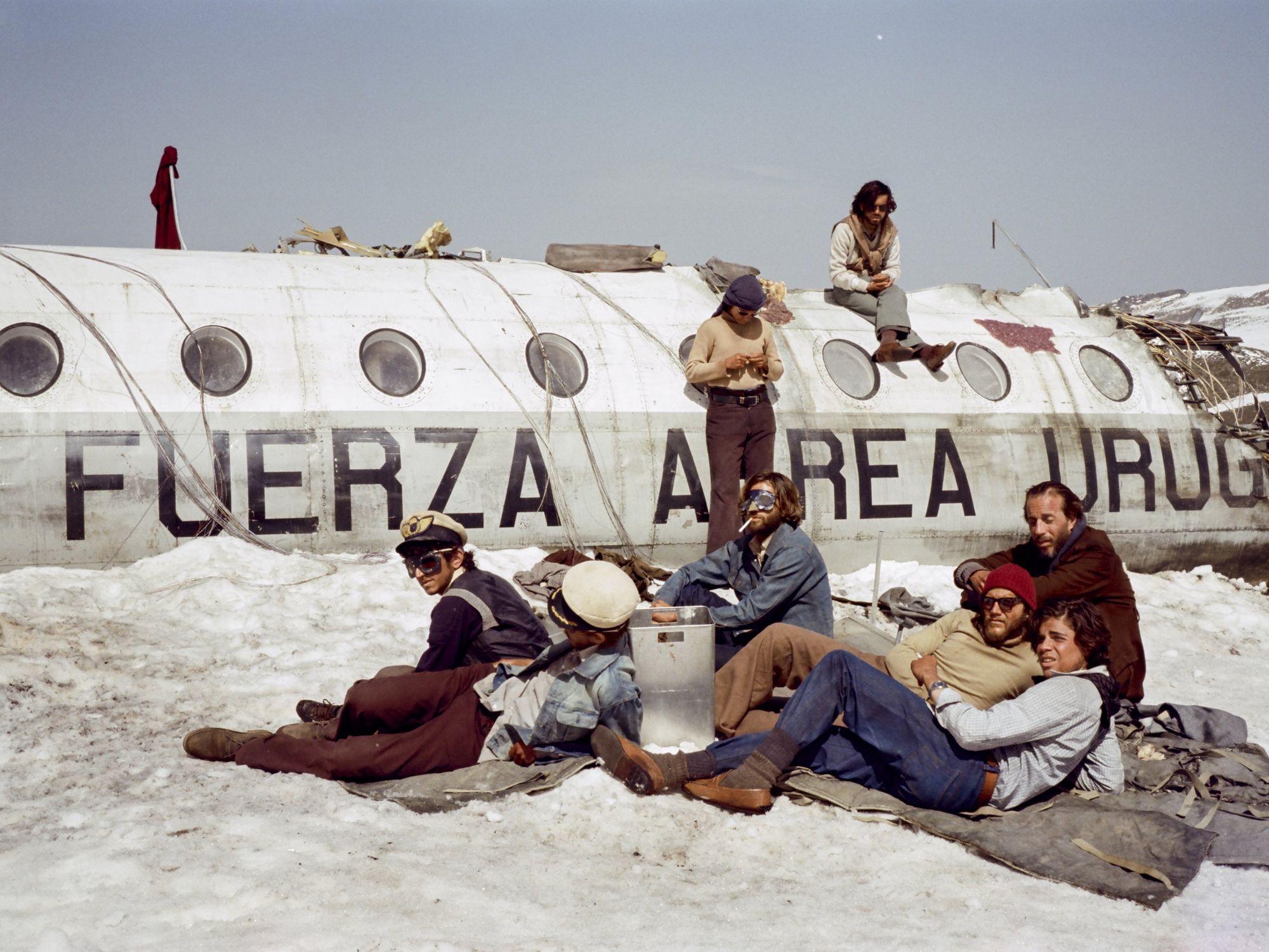 people sitting on mats on snow alongside a crashed airplane