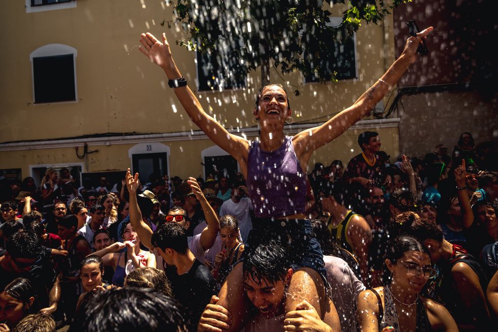 People take part in the traditional refreshing water battle demanding water from the neighbors on their balconies in a centric street of Es Castell during their Sant Jaume festival while the island is still suffering high temperatures.
