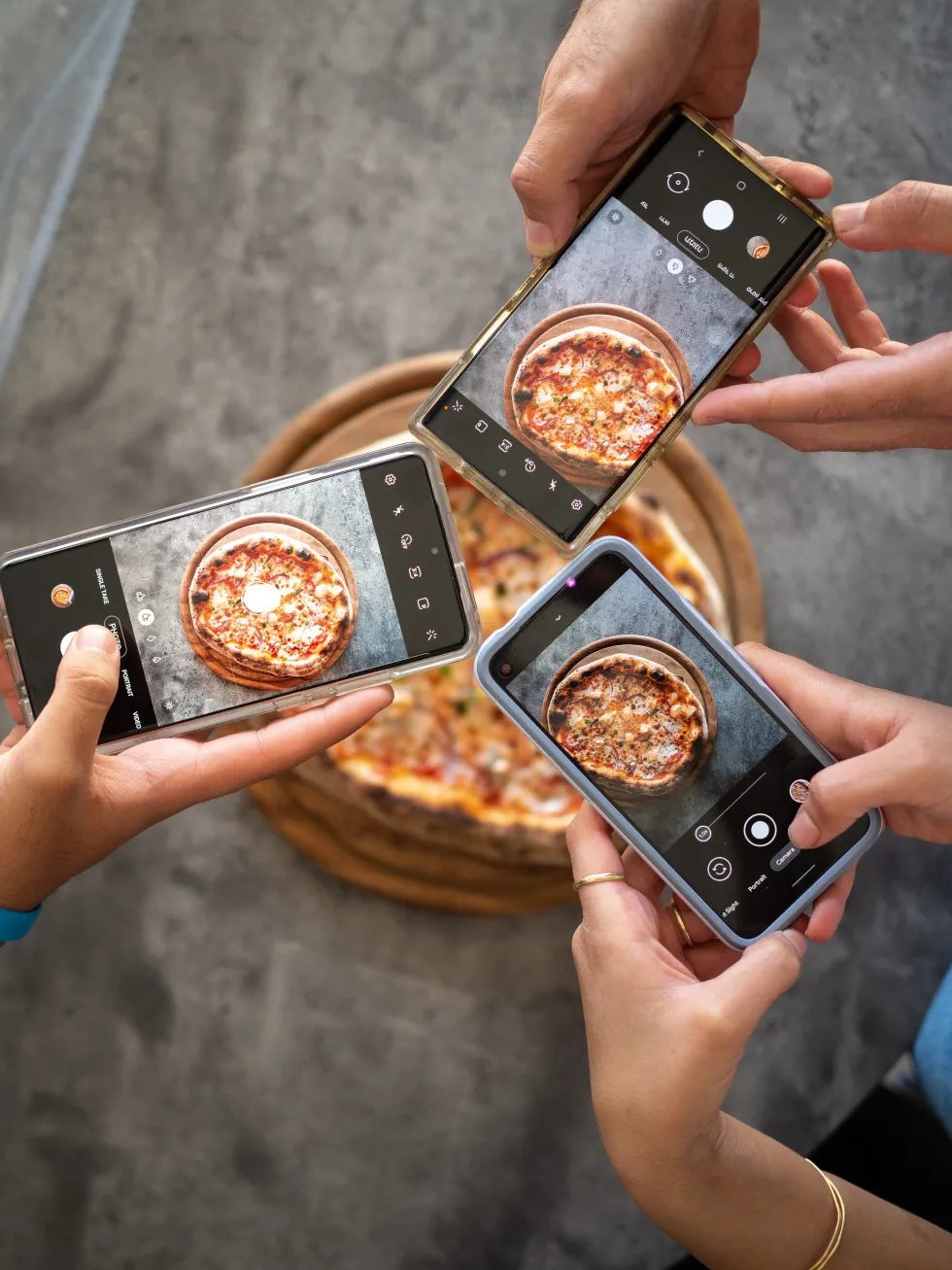 People taking pictures of a pizza with smartphones.​
