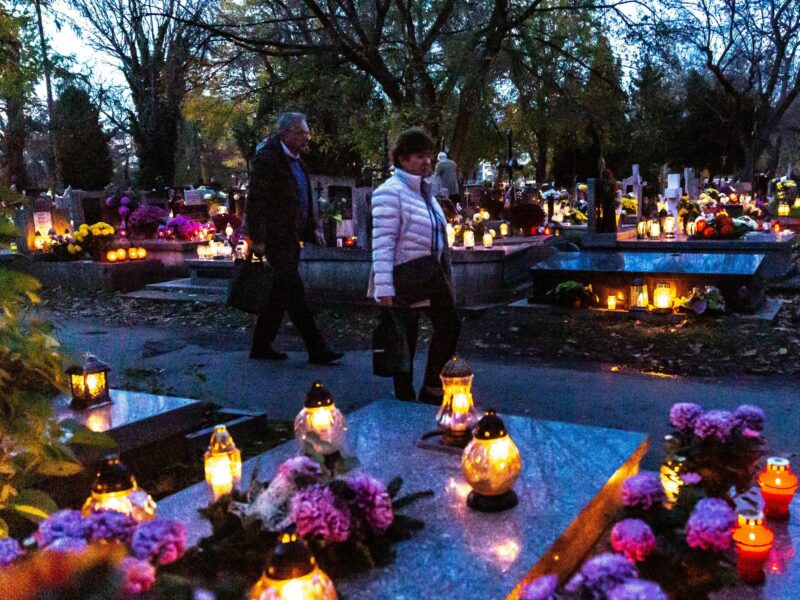 People walk between graves decorated with flowers and candles