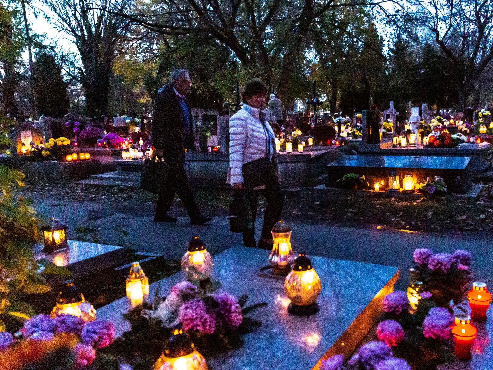 People walk between graves decorated with flowers and candles