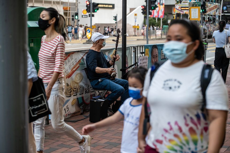 People walk by a musician playing 'Glory to Hong Kong' on the street in Hong Kong.