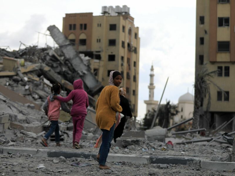 People walk past destroyed buildings in the central Gaza Strip, on March 25, 2024.