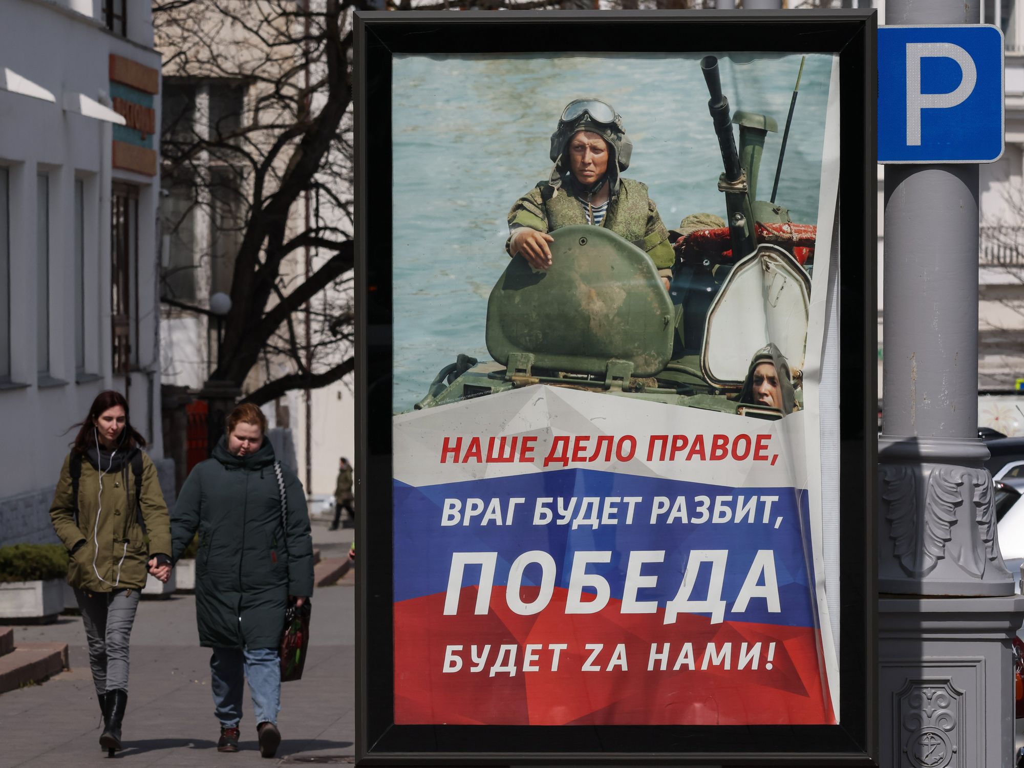 People walking by a Russian army poster on Ushakova Square in Sevastopol, Crimea