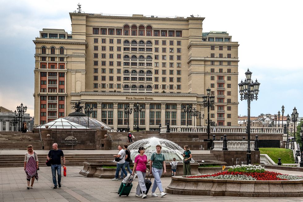 People walking together in front of a big building with a fancy veranda and a flower bead in the middle of the square