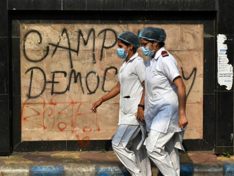 photo of 2 nurses in india walking past graffiti that says "democracy'