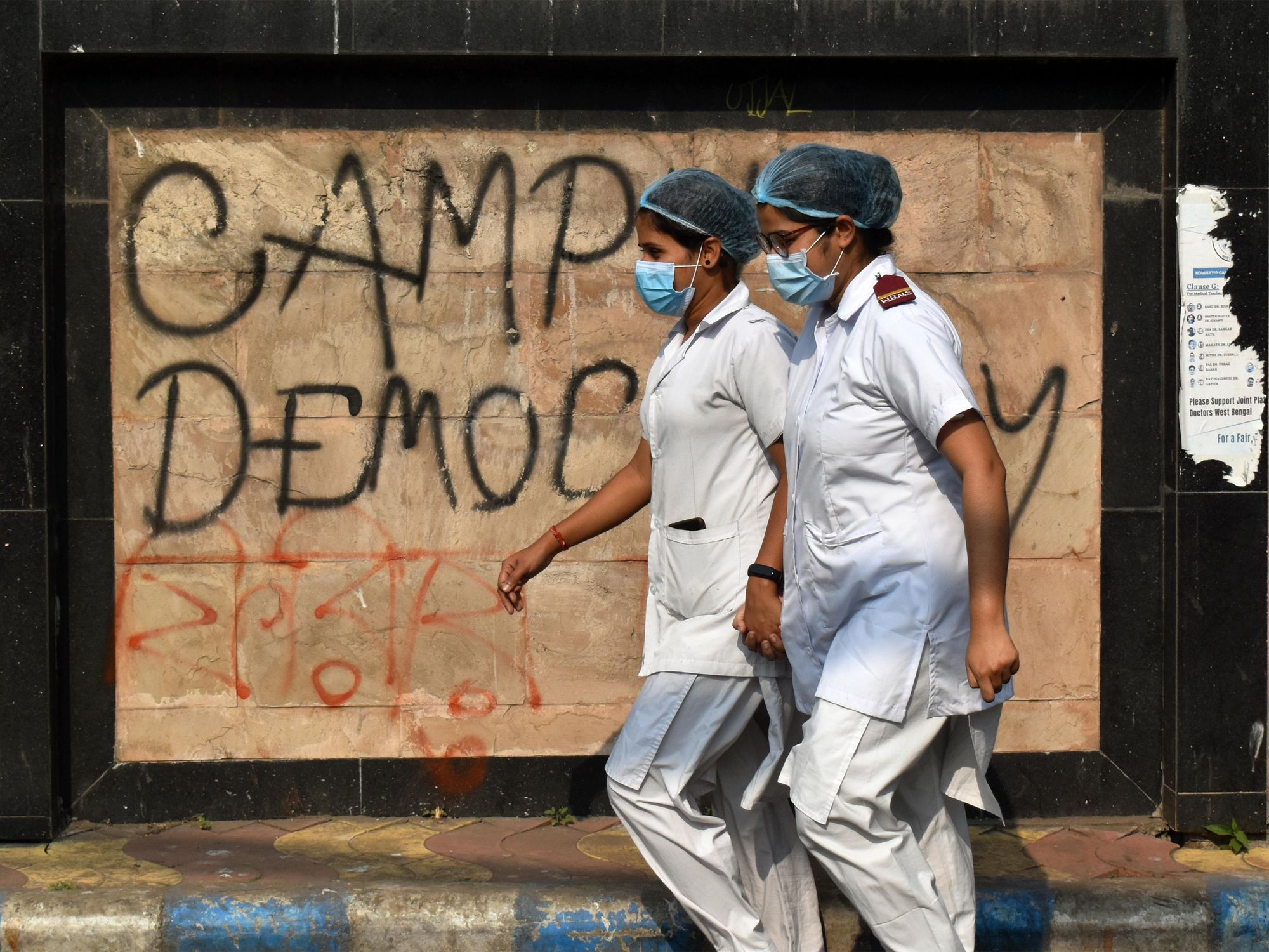 photo of 2 nurses in india walking past graffiti that says "democracy'
