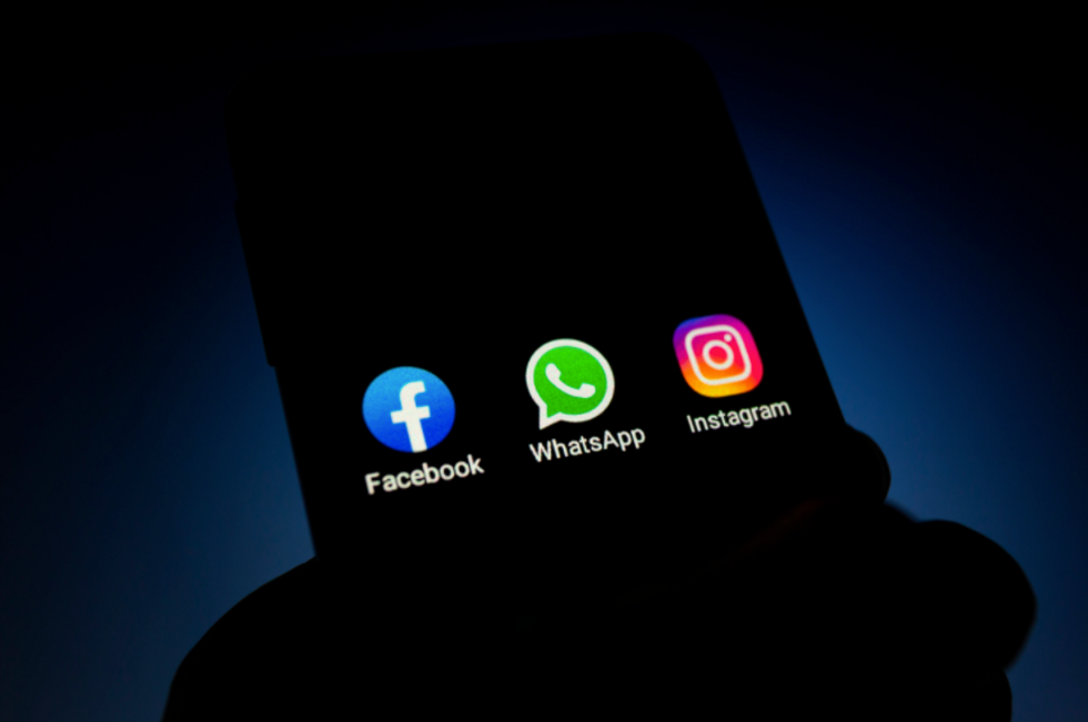Photo of a backlit hand holding a smart phone with Facebook, WhatApp and Instagram icons on the screen.