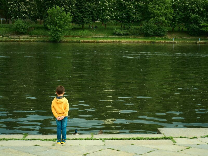 photo of a boy from behind looking at a pond
