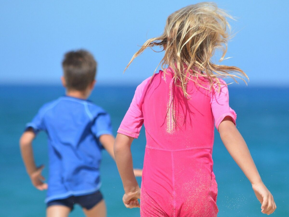 Photo of a boy wearing blue and a girl wearing pink running toward a body of water