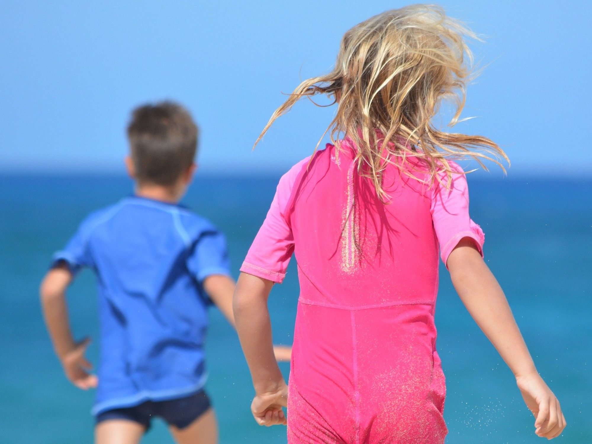 Photo of a boy wearing blue and a girl wearing pink running toward a body of water