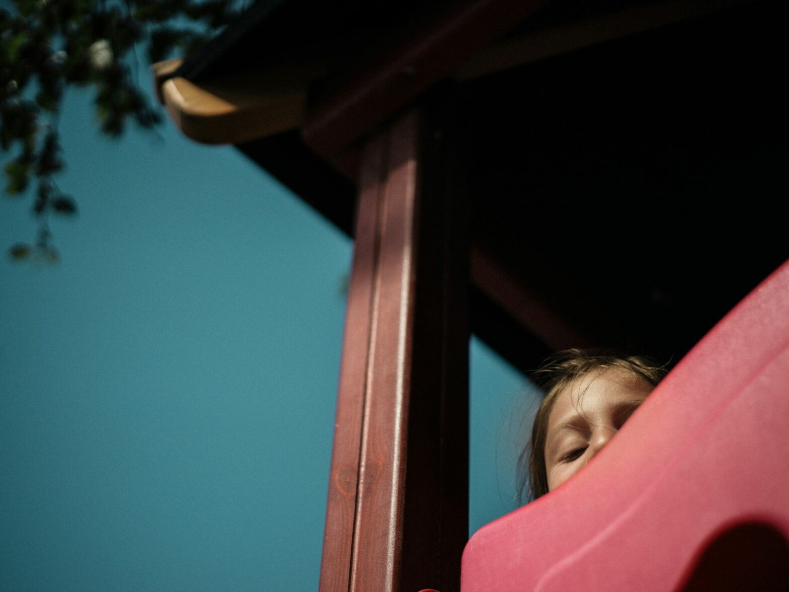Photo of a child peeking from the top of a slide at a playground
