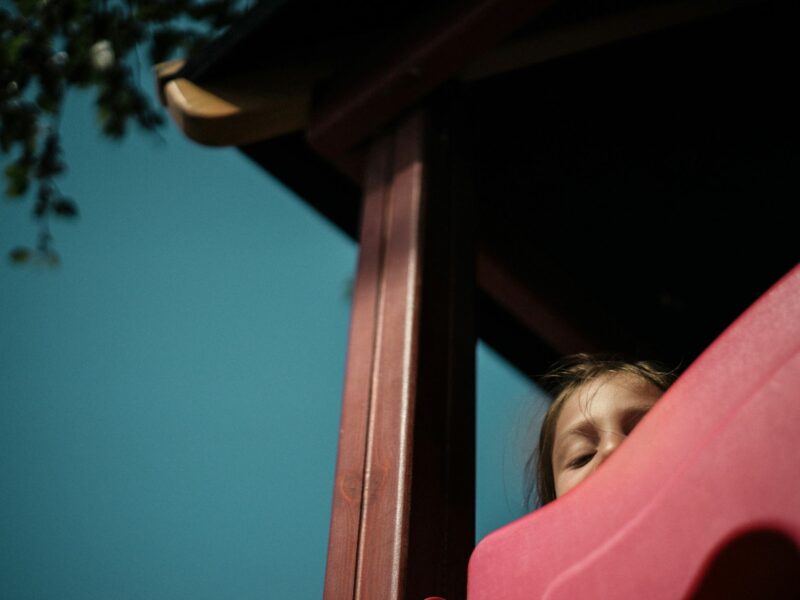Photo of a child peeking from the top of a slide at a playground