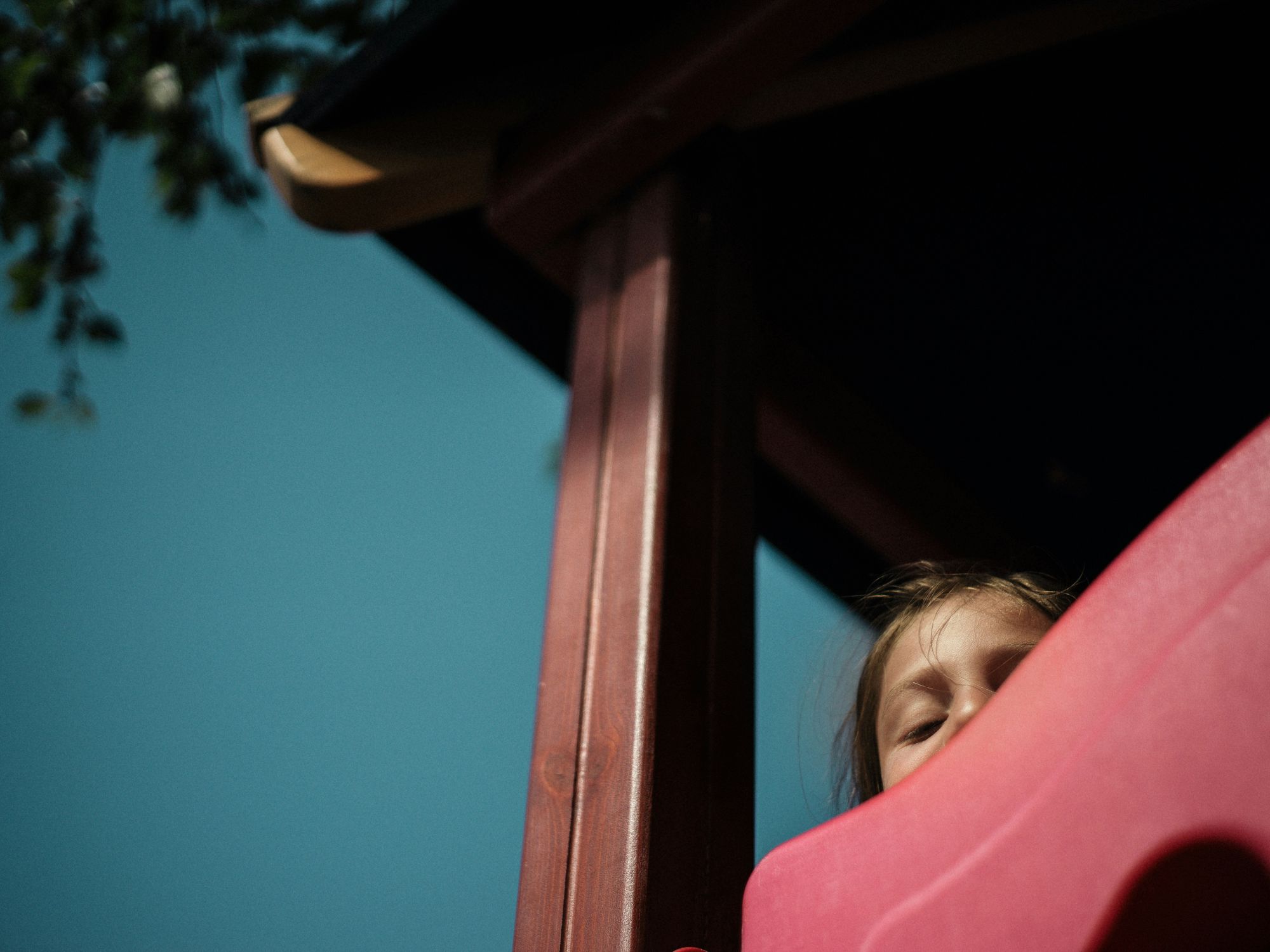 Photo of a child peeking from the top of a slide at a playground