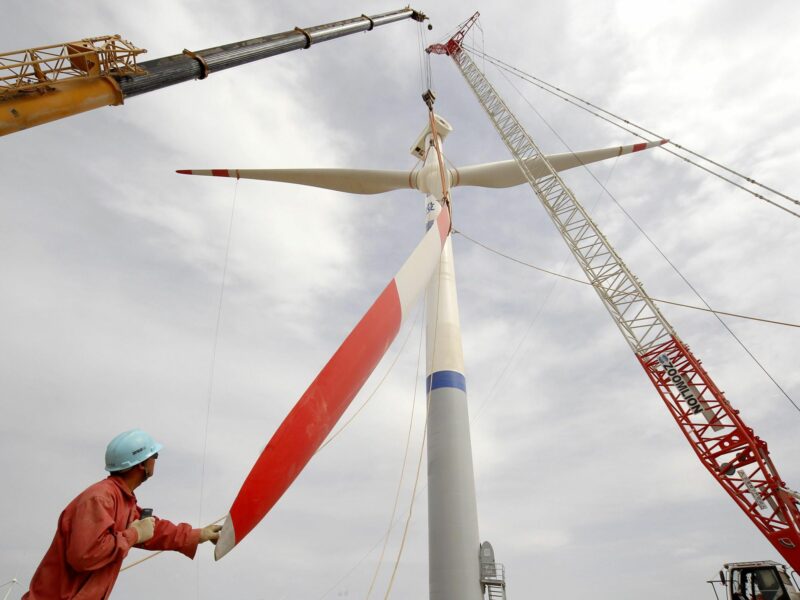 Photo of a Chinese worker holding the blade of a wind turbine being built by cranes in Hami, Xinjiang, China