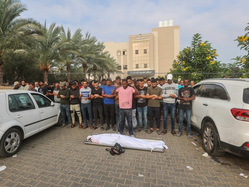 photo of a corpse wrapped in a sheet and people praying