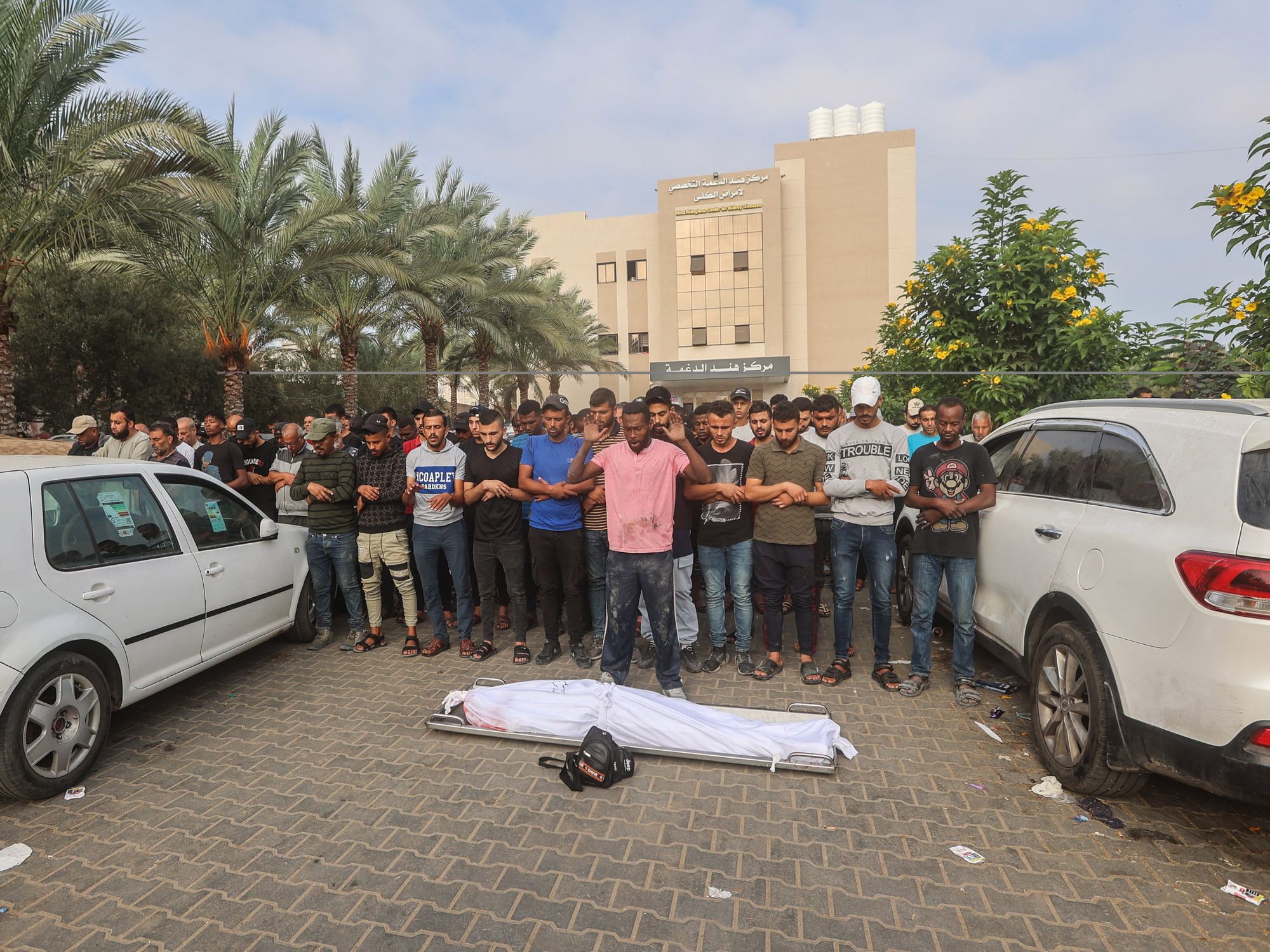 photo of a corpse wrapped in a sheet and people praying