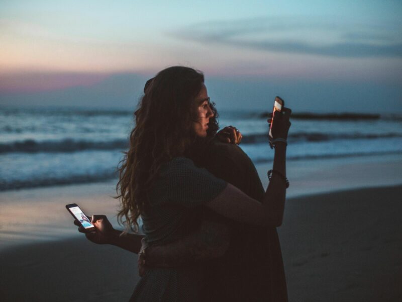 Photo of a couple checking their phones while sharing an embrace on a beach