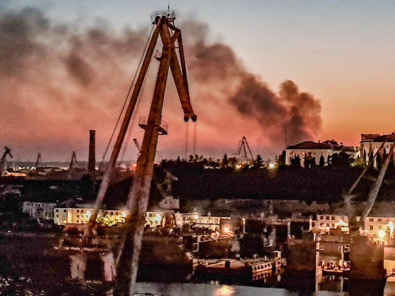 photo of a crane, a shipyard and smoke in the distance