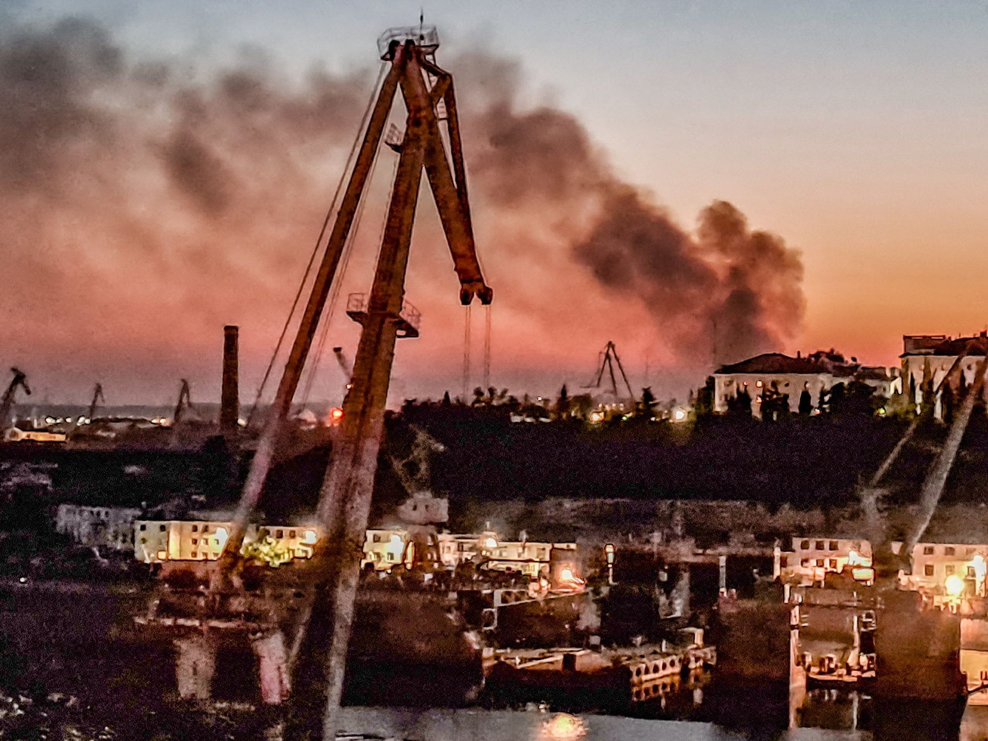 photo of a crane, a shipyard and smoke in the distance