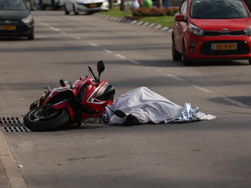 photo of a crashed motorcycle and a covered dead body