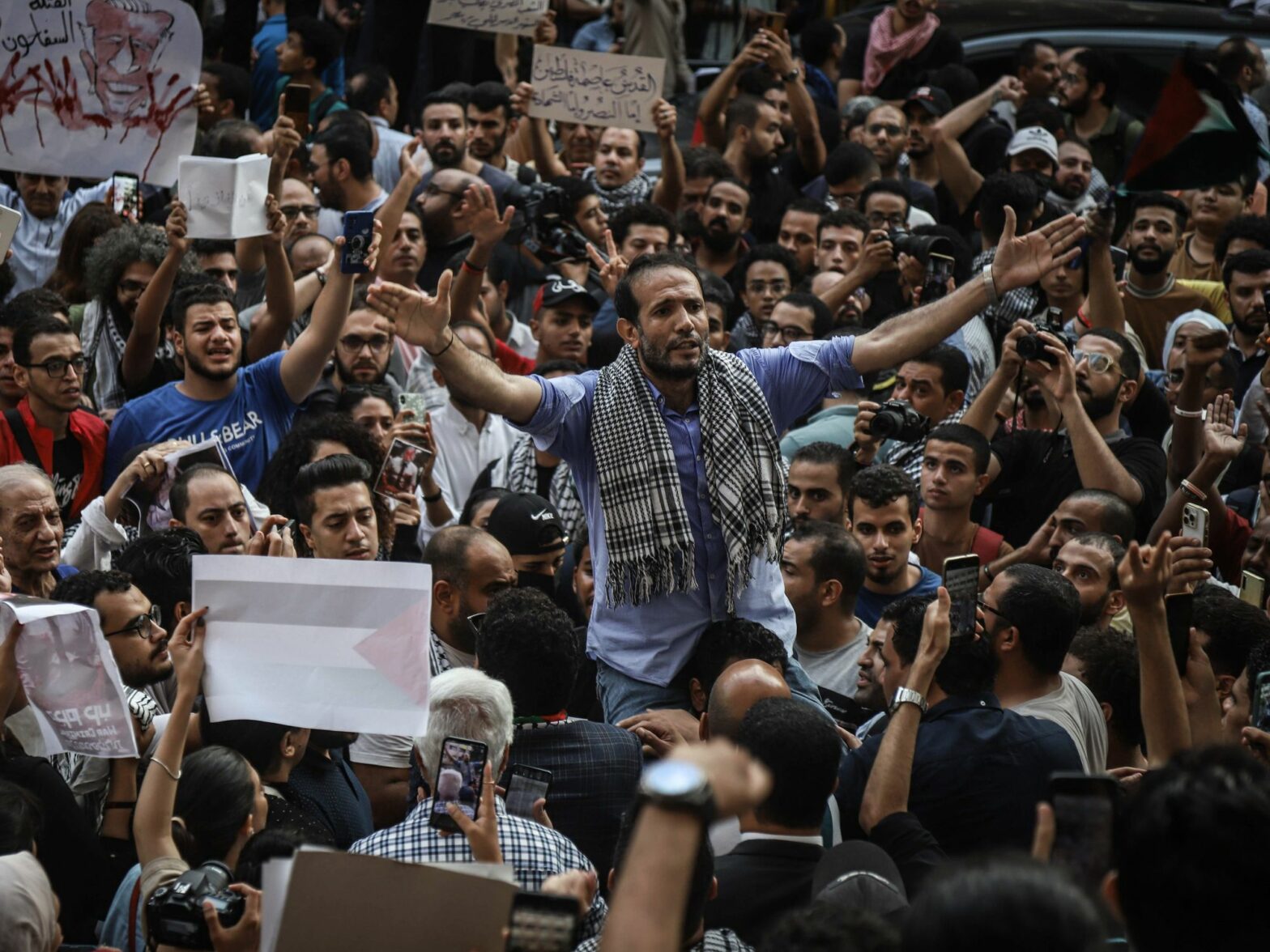 photo of a crowd of protesters holding signs and holding up their arms