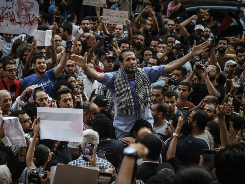photo of a crowd of protesters holding signs and holding up their arms