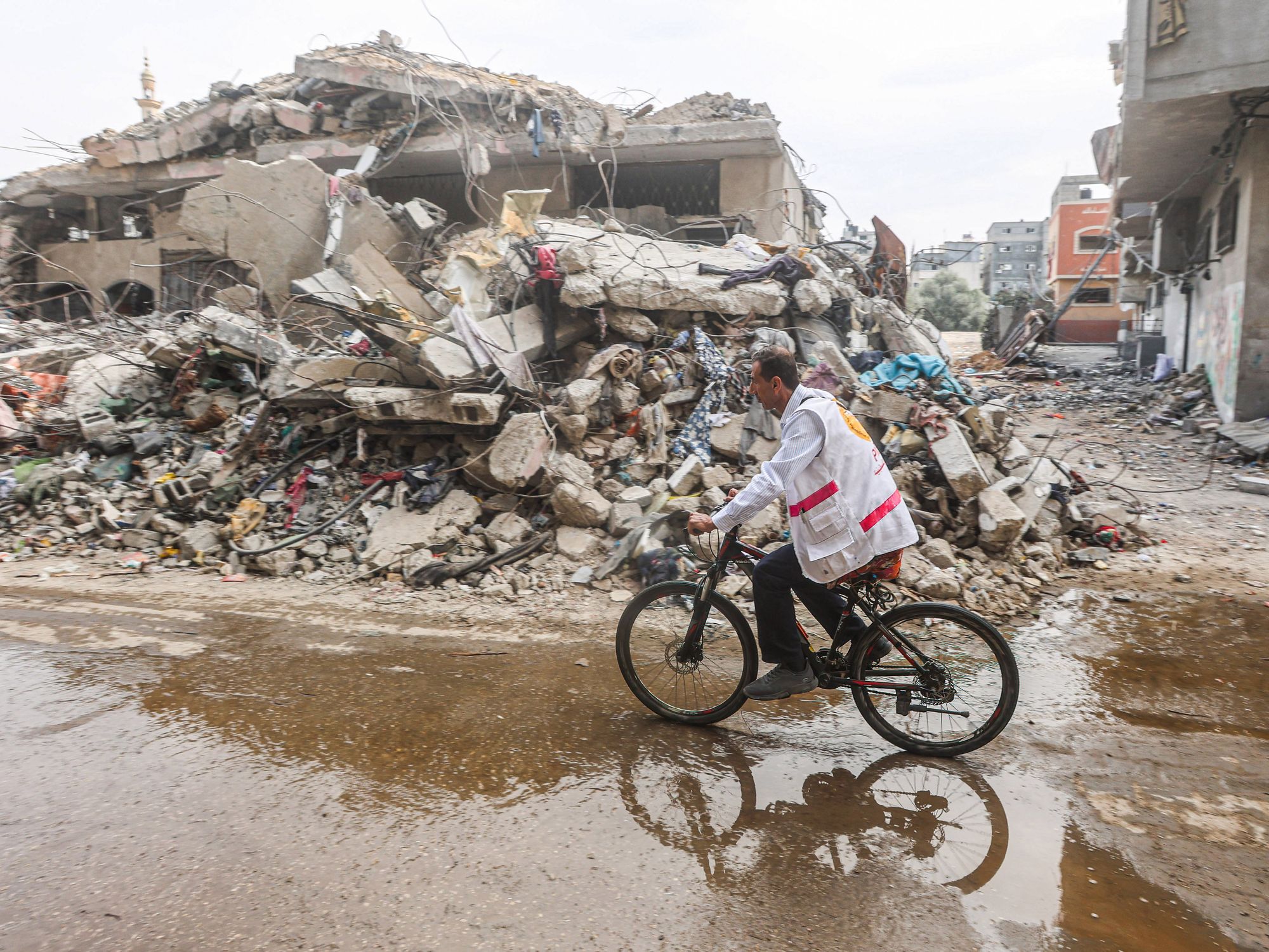 Photo of a doctor riding his bicycle past debris in Al-Bureij camp in central Gaza