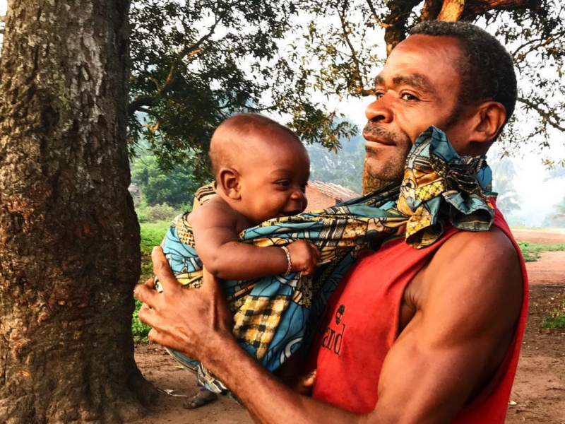 Photo of a ​man from the Aka tribe carrying his infant son