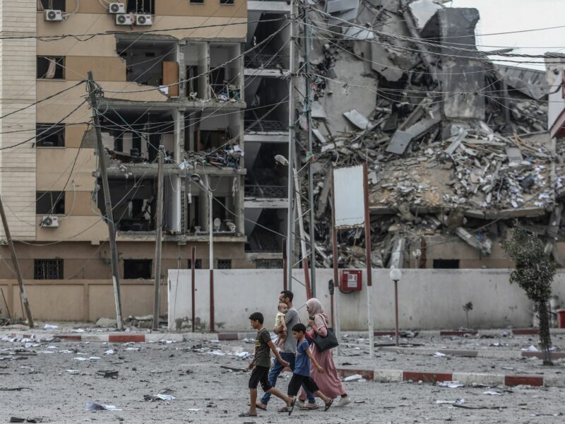 photo of a family of five walking past a bombed out building