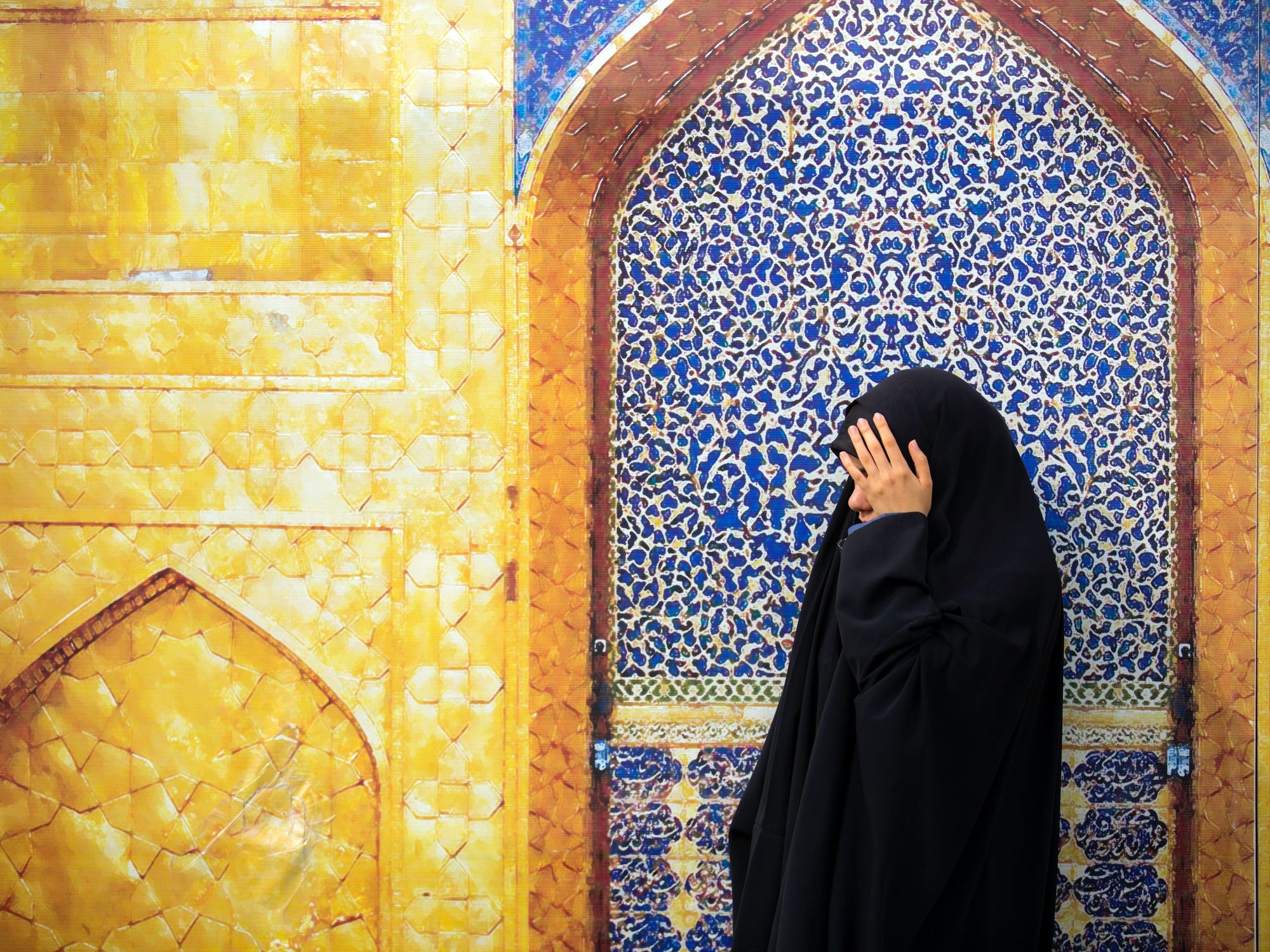 Photo of a girl hiding her face in front of a mosque in Mehran, Iran