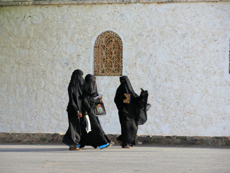 Photo of a group of three veiled women walking past a mosque in Taiz, Yemen.