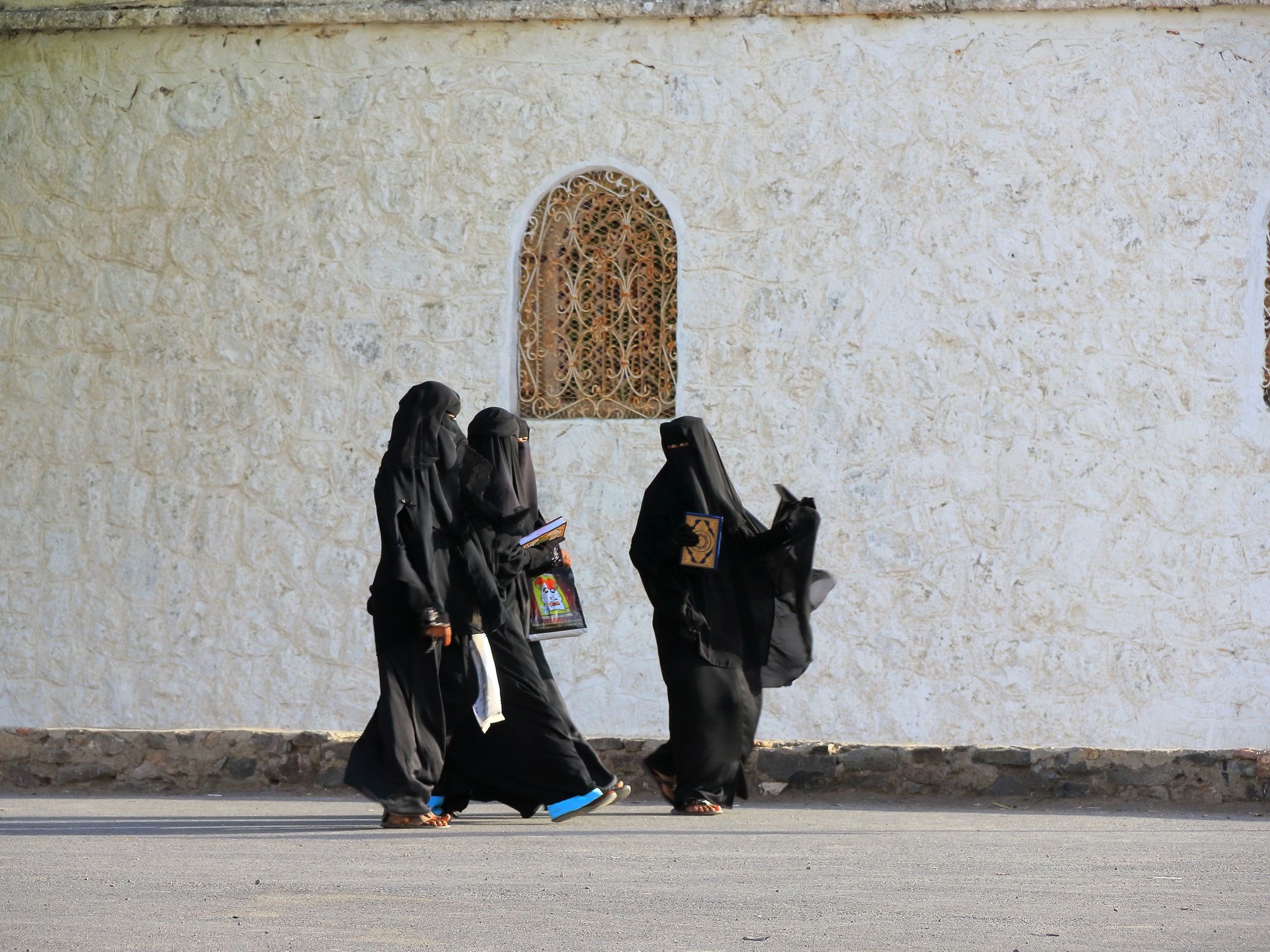 Photo of a group of three veiled women walking past a mosque in Taiz, Yemen.