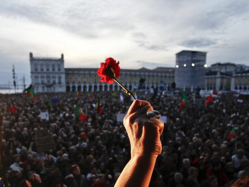 Photo of a hand brandishing a carnation flower in a crowded square in Portugal