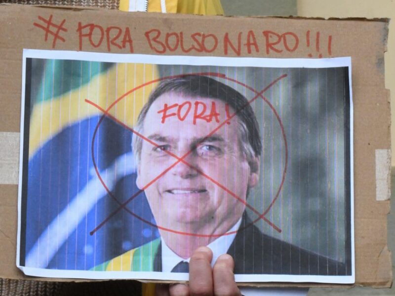 Photo of a hand holding a sign with Brazilian President Jair Bolsonaro's face, with the slogan "Out Bolsonaro!!!"