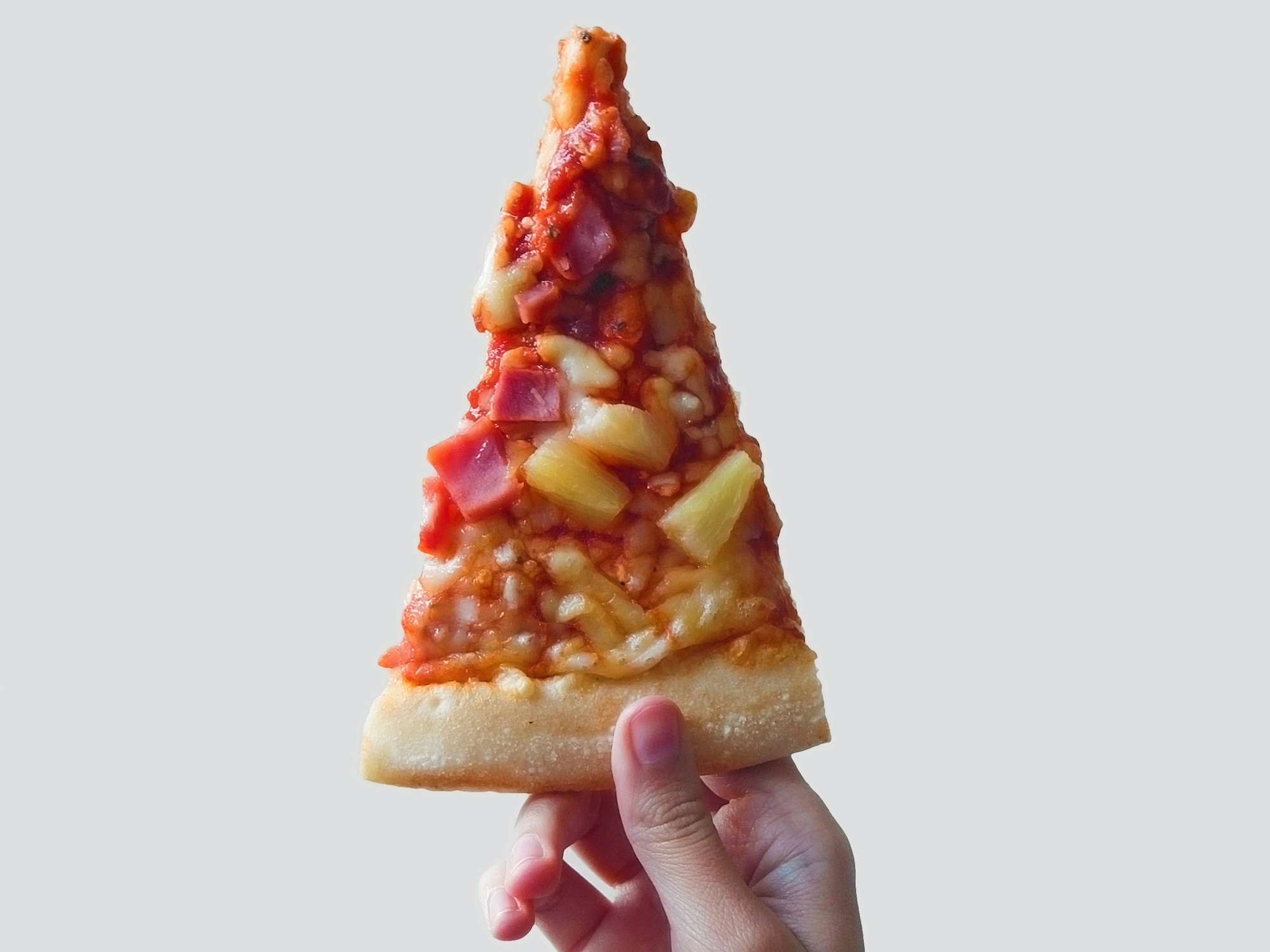 Photo of a hand holding a slice of Hawaiian pizza