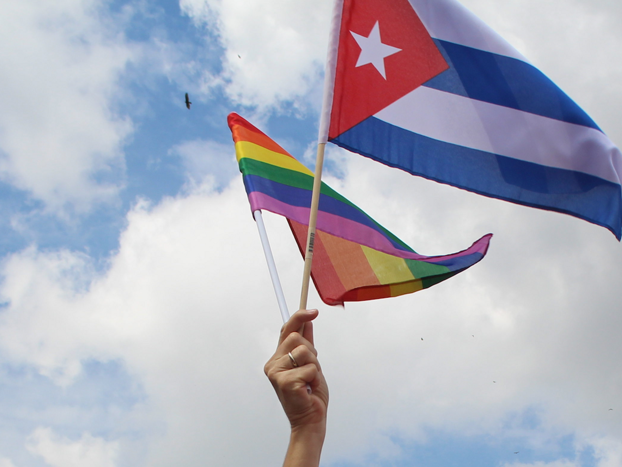 Photo of a hand waving a rainbow flag and a Cuba flag at a pro-LGBTQ+ rights demonstration in Havana, Cuba