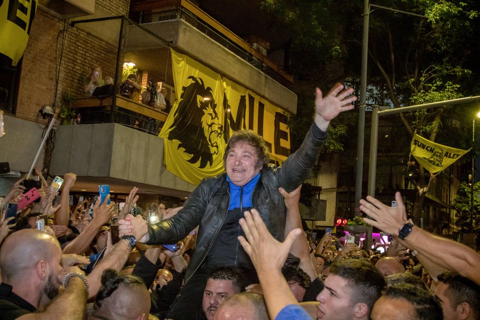Photo of a large crowd celebrating the conclusion of Javier Milei election campaign. They hold him up as he waves to the crowd and cell phones record him from every direction.