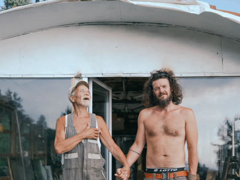 Photo of a man and his adult son holding hands. The father is laughing.