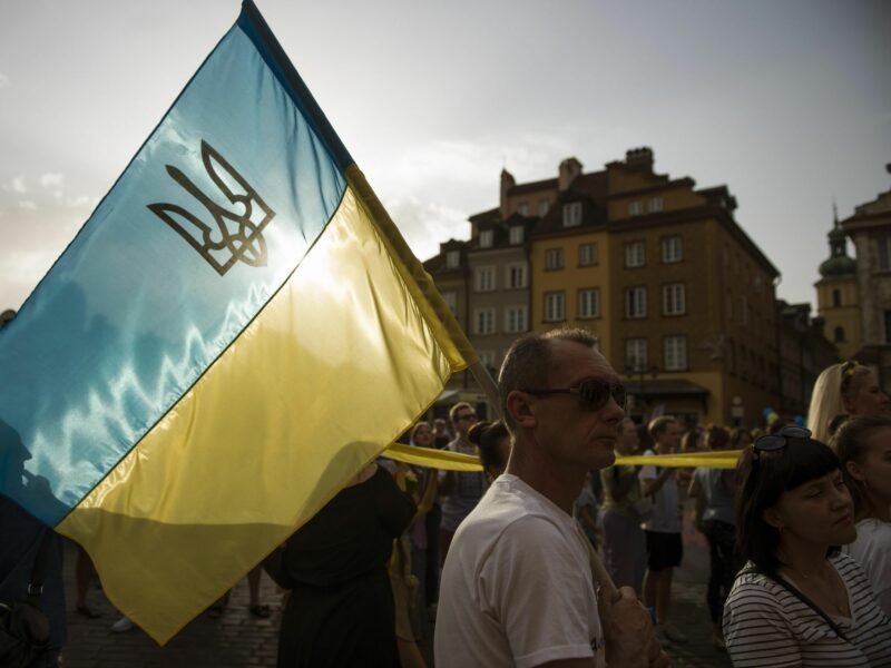 photo of a man carrying a ukrainian flag at a rally in Warsaw