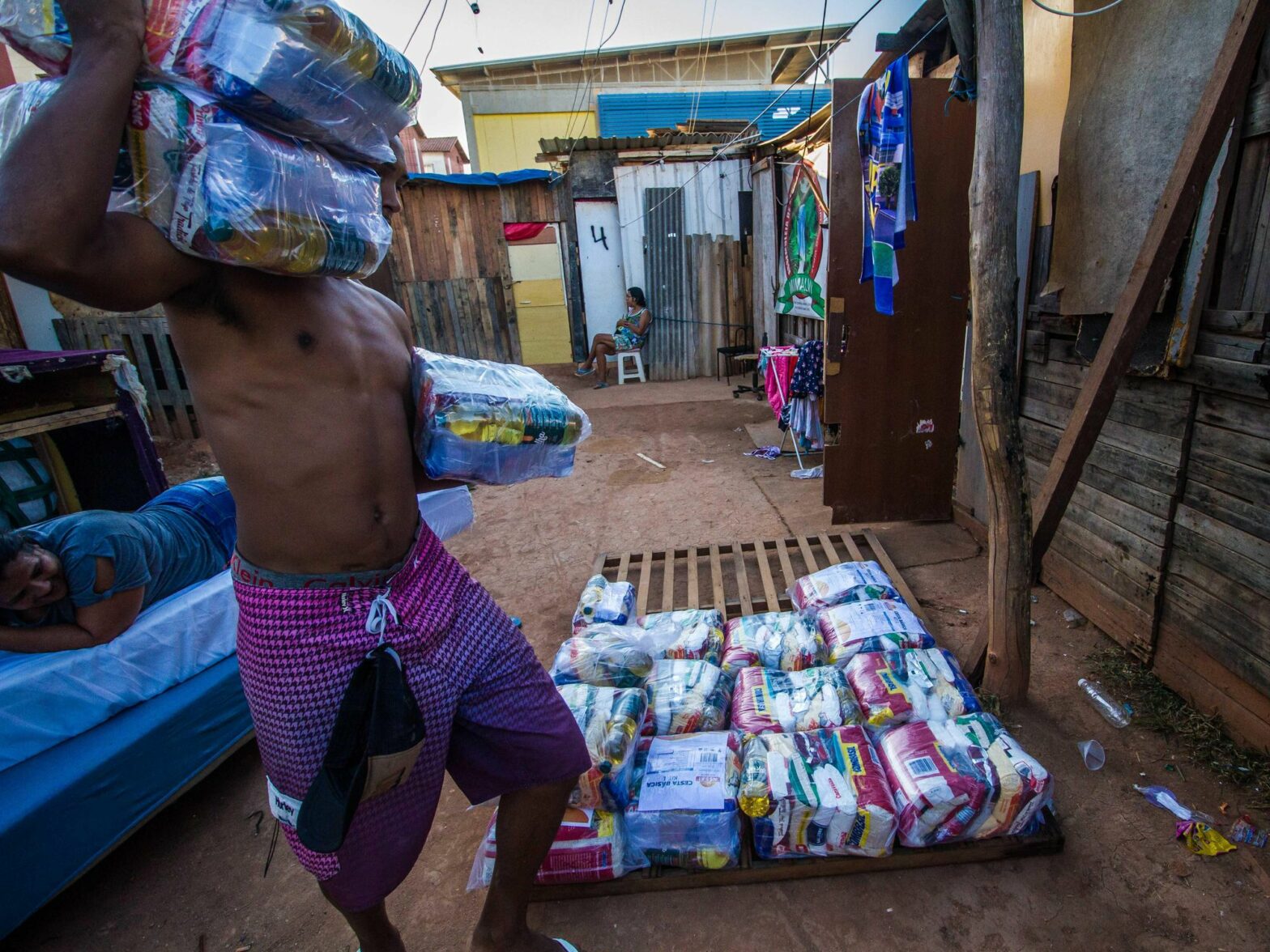 Photo of a man carrying food packages as residents of a favela in Santa Cruz, Brazil, receive aid.