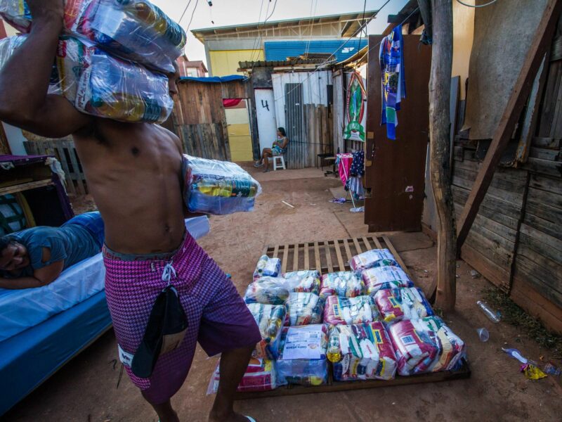 Photo of a man carrying food packages as residents of a favela in Santa Cruz, Brazil, receive aid.