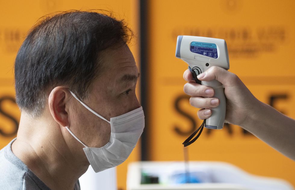 Photo of a man getting his temperature checked before entering the cinema as businesses are reopening in Hong Kong